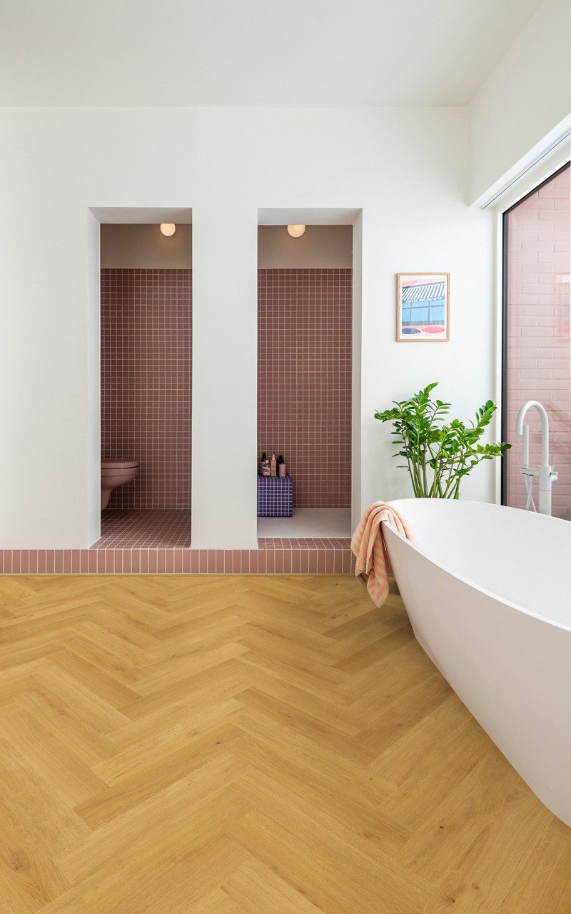 Herringbone laminate floor Quick Step Impressive Design Cumin Oak, installed on bathroom floor with a white bathtub