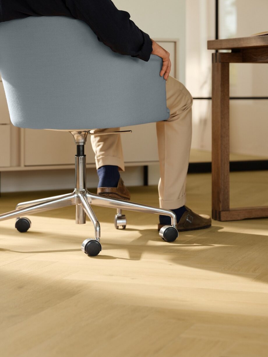 laminat-quick-step-impressive-design-nutmeg-oak Laminat Quick Step Impressive Design Nutmeg Oak, verlegt im Büro, blauer Bürostuhl mit sitzendem Mann