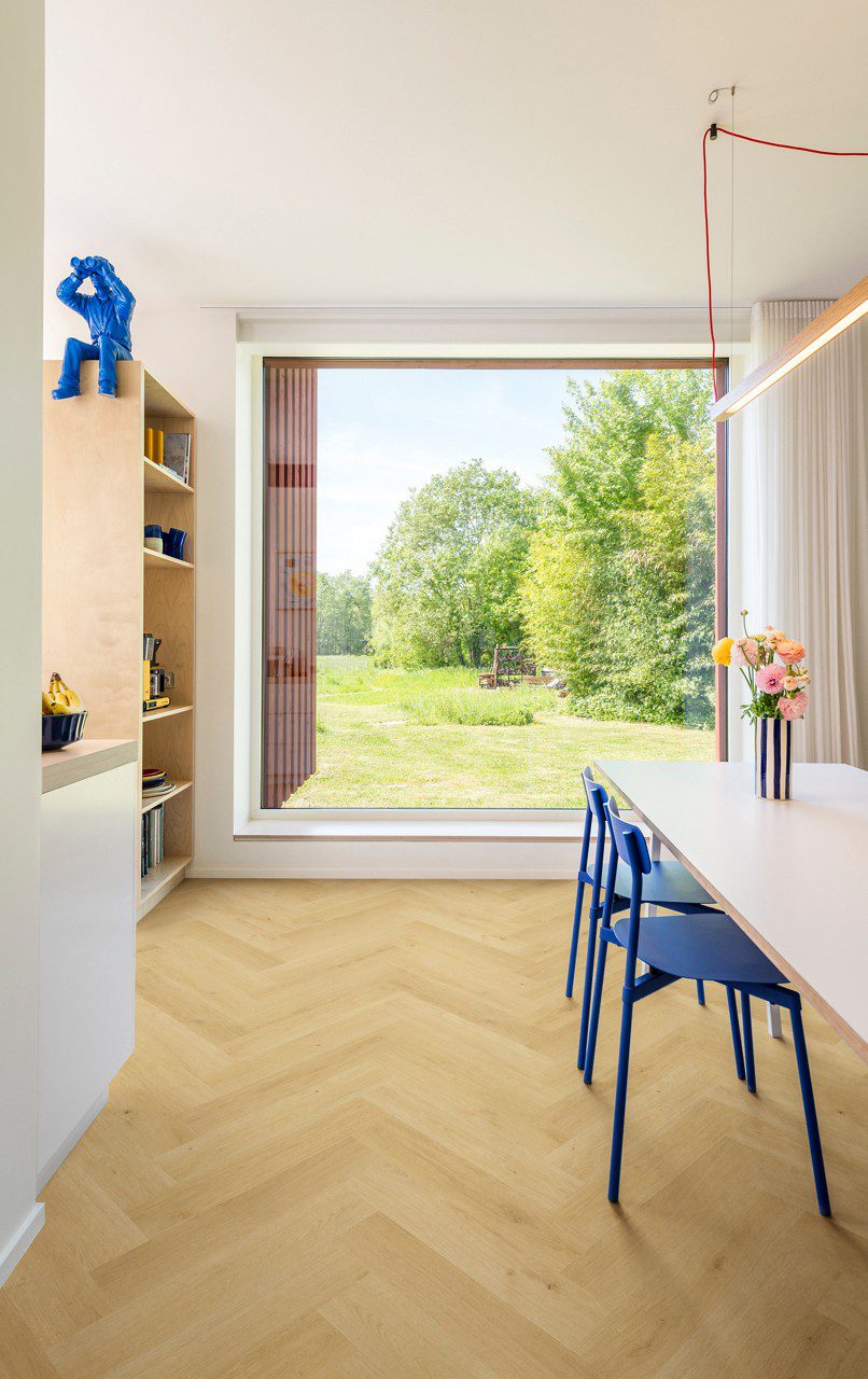 Ламинат ёлочкой Quick Step Impressive Design Nutmeg Oak, уложен на кухонный пол, белый обеденный стол с синими стульями и вазой с цветами