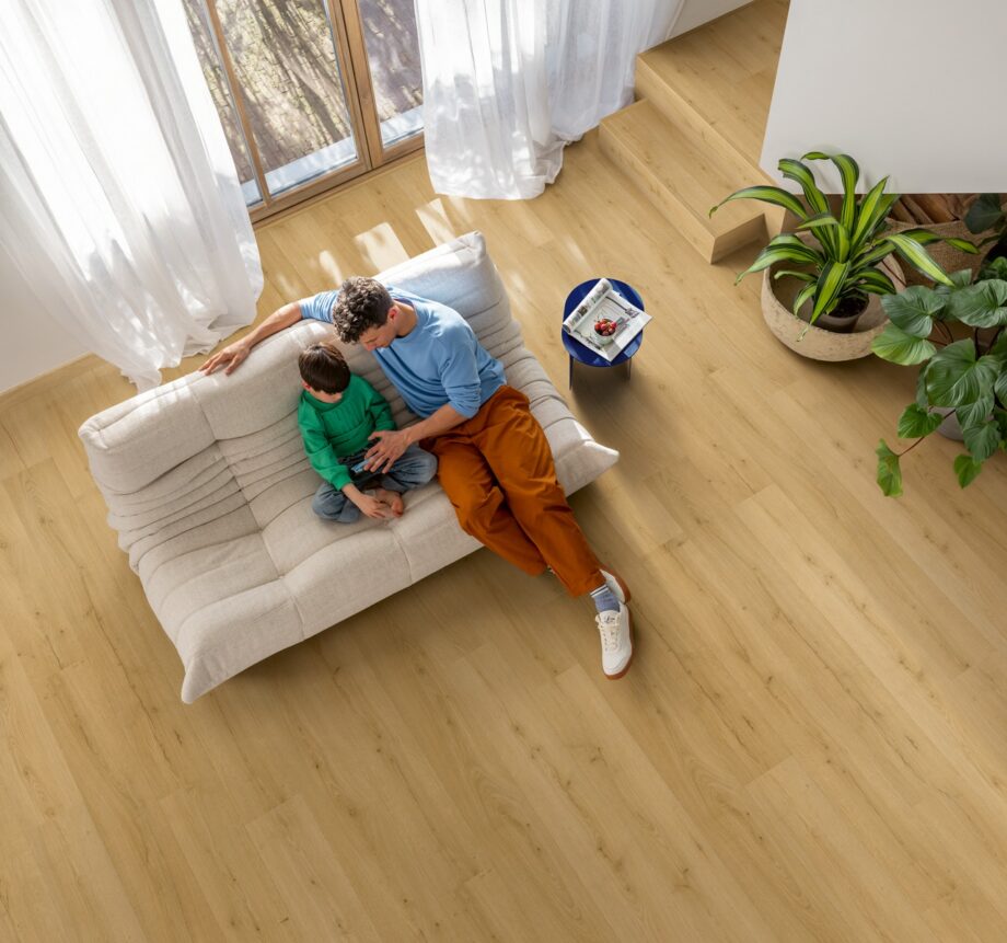 LVT floor Quock-Steü Bloom Brushed Oak Honey installed on the Livingroom floor: Father and son watching a phone on a sofa.