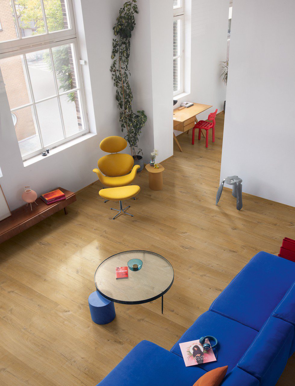 LVT flooring Quick-Step Bloom Cotton Oak Deep Natural installed on a livingroom floor. Blue sofa, sofa table, yellow chair.