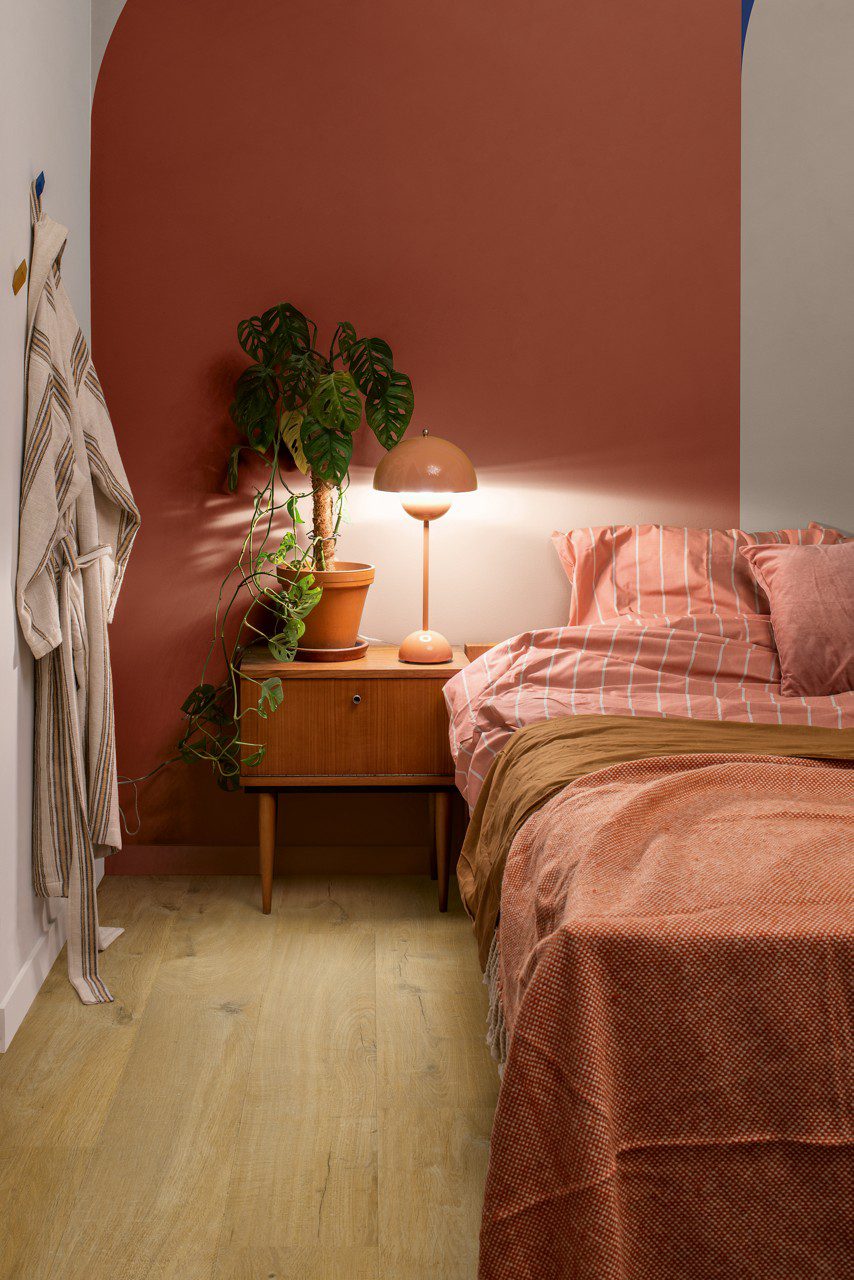 LVT põrandakate Quick-Step Bloom Cotton Oak Deep Natural paigaldatud magsmistoa põrandale. Voodi, öökapp, lamp öökapil.