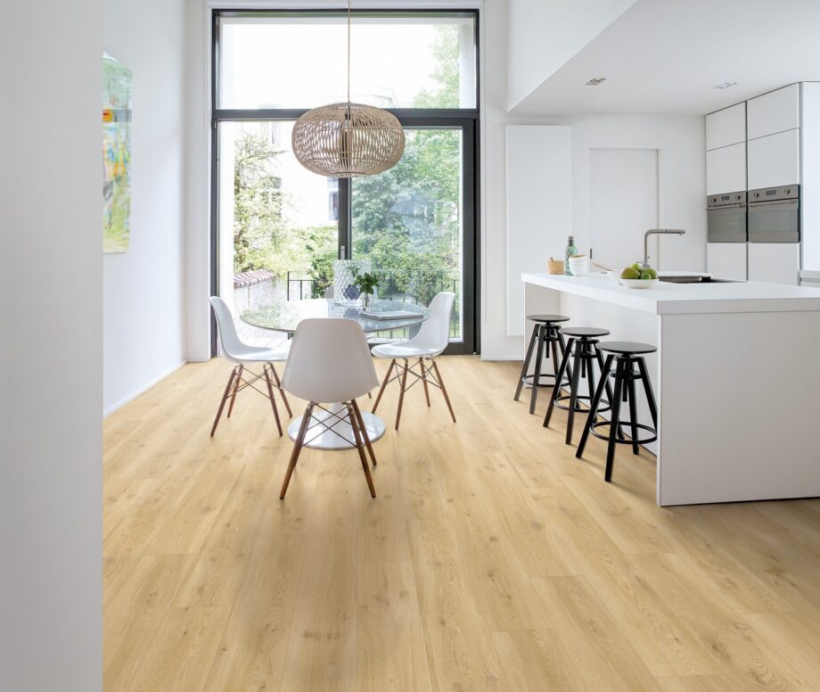 LVT põrandakate Quick-Step Blos Drift tamm beige paigaldatud köögi põrandale. Valge köögimööbel, köögisaar koos musta värvi toolidega. Ümar söögilaud koos valgete toolidega.