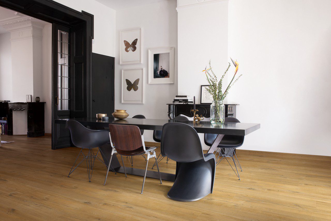 Виниловый ламинат Quick Step Bloom Cotton Oak Deep Natural уложен на полу в столовой, современный обеденный стол с каменной столешницей, стулья вокруг стола, на столе цветы.