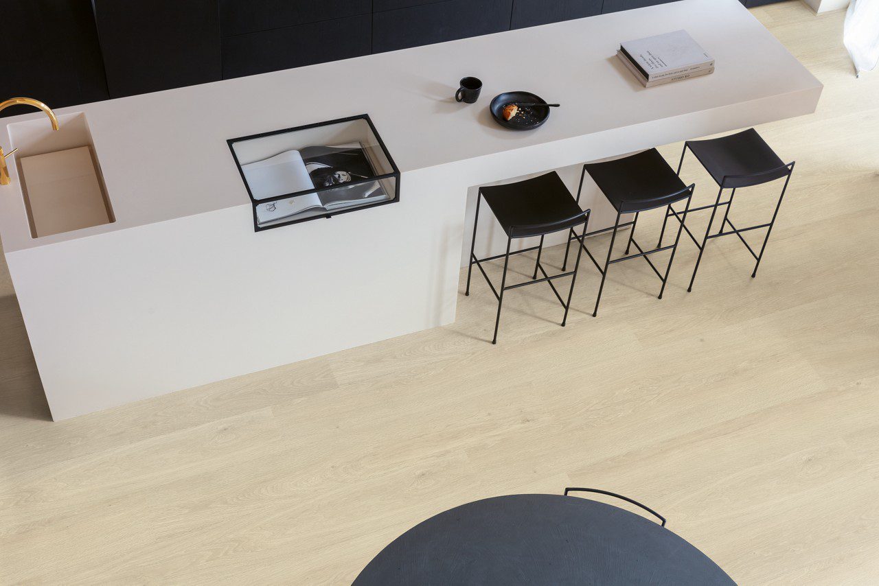 Виниловый ламинат Quick Step Bloom Sea Breeze Oak Beige уложен на полу на кухне, стильный каменный кухонный остров и стулья.