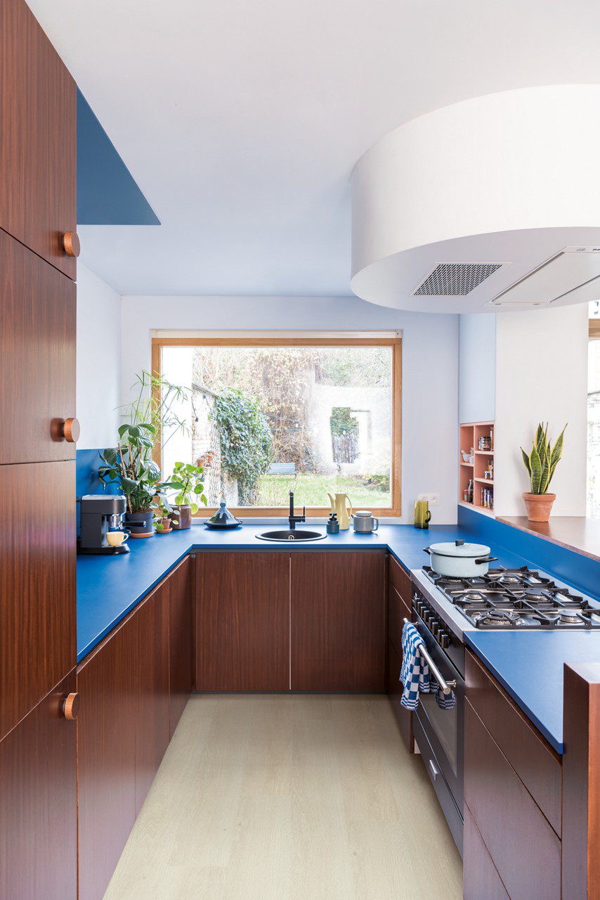 Виниловый ламинат Quick Step Bloom Sea Breeze Oak Light уложен на полу на кухне, кухонная мебель с синей столешницей и коричневыми фасадами.