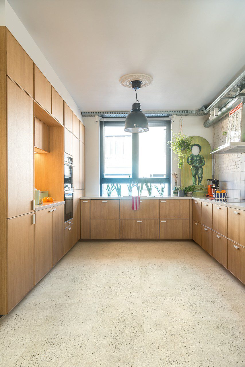 Klick-Vinyl mit Trittschalldämmung Quick-Step Illume Pebble Concrete, verlegt auf dem Küchenboden – moderne Küchenmöbel und eine helle Betonoptik.