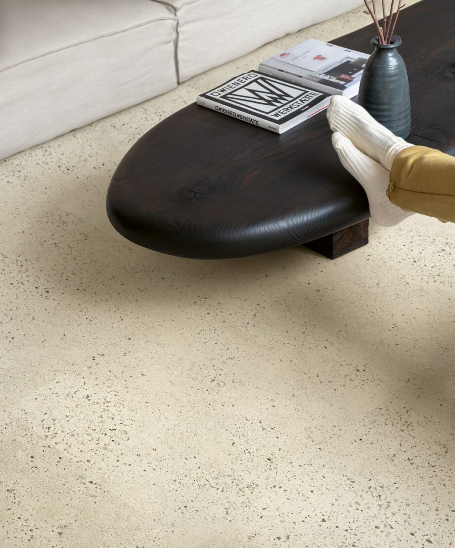 lvt-porand-quick-step-illume-pebble-concrete LVT põrand Quick-Step Illume Pubble concrete paigaldatud elutoa põrandale. Madal telekalaud milelel keegi toetab oma jalgu. Laual on lisaks jalgadele ka raamatud ja vaas.