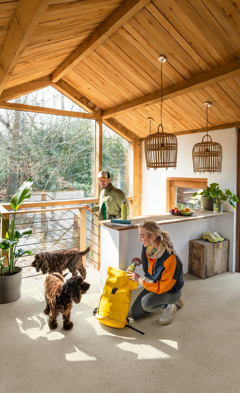 LVT Quick-Step Illume Pebble concrete paigaldatud elutoa põrandale. Naine kükitab ja võtab kollasest seljakotist midagi. Kaks vahvat koera. Mees tuleb trepist ülesse.