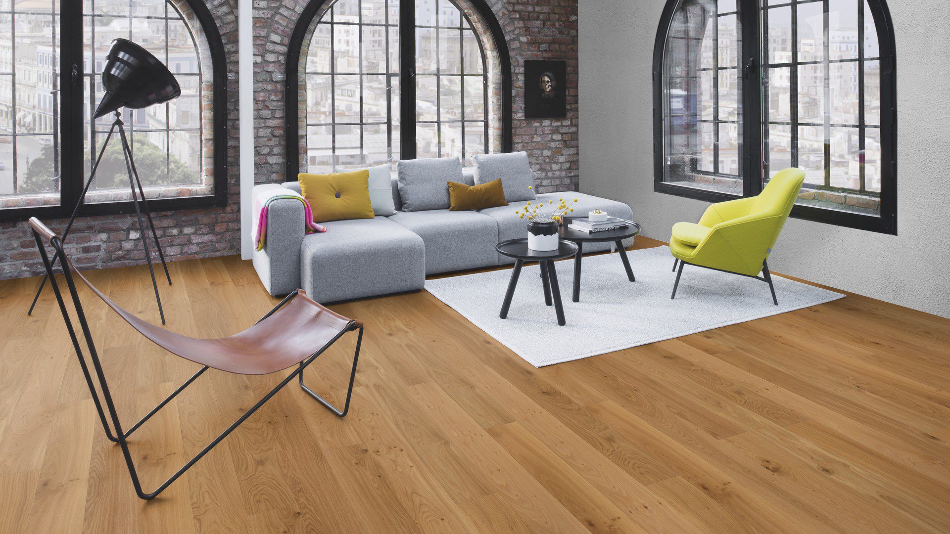 Parketti Bauwerk Casapark Budget Cut tammi 35, harjattu ja öljyvahattu, asennettuna olohuoneen lattialle – harmaa sohva, kaksi tummaa pyöreää sohvapöytää ja niiden alla harmaa matto. Luonnollinen, lämminsävyinen tammensävy ja kevyesti rustiikkinen sorteerus (maltillisesti oksakohtia ja hienovaraista sävyvaihtelua).