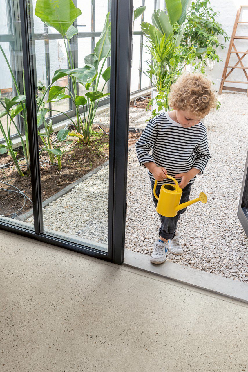 LVT flooring tiles Quick-Step Illume Oyster concrete with light grey color installed in hallway and kid is coming inside from summer garden.