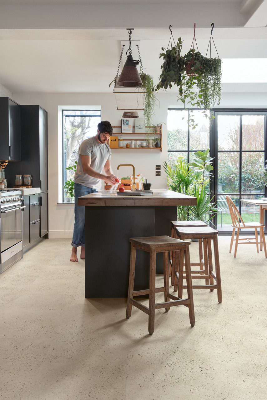Vinyl flooring tiles Quick-Step Illume Pebble concrete installed on a kitchen floor. Man is washing apples.