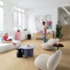 Klick Vinyl Fischgrat Quick Step Ciro Pure Oak Blush, verlegt auf dem Wohnzimmerboden und auf der Treppe mit farblich passender Incizo-Leiste. Eine Frau liegt auf einem weißen Sofa und unterhält sich mit einem Mann, der auf dem Boden steht.