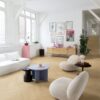 Виниловый ламинат Quick-Step Ciro Pure Oak Blush, уложен на полу и лестнице в гостиной с использованием плинтусов Incizo. Белый диван, белые кресла, небольшие круглые журнальные столики и комод.