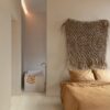 klickvinyl-quick-step-bloom-sea-breeze-oak-light Klickvinyl Quick Step Bloom Sea Breeze Oak Light im Schlafzimmer verlegt, sehr heller Eicheton und Dielendesign, Bett mit schöner hellbrauner Bettwäsche, im Hintergrund ein Badezimmer mit freistehender, eckiger Design-Badewanne.