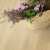 lvt-floor-quick-step-bloom-botanic-beige LVT floor Quick-Step Bloom Botanic Beige installed on a floor. On the floor is laying open bag with many different beautiful pink flowers.