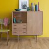 Rigid Vinylboden Quick Step Bloom Cotton Oak Natural im Wohnzimmer verlegt, gelbe Wand und klassischer Vitrinenschrank.