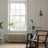 Quick Step Blos Buttermilk Oak vinyl floor installed in a living room, with a classic wall radiator, a rocking chair, white classic wall panels, and potted plants.
