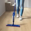 vinylboden-quick-step-bloom-botanic-beige Vinylboden Quick Step Bloom Botanic Beige im Flur verlegt, eine Frau reinigt den Boden mit einem Wischmopp.