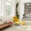 vinyylilattia-quick-step-blos-vaalea-canyon-tammi-beige Vinyylilattia Quick Step Blos Vaalea Canyon Tammi Beige asennettuna olohuoneen lattialle ja kirjanurkkaan johtaville porrasaskelmille, vaalea hiekanbeige tammen sävy ja lankkudesign, keltainen lepotuoli jalkarahilla, lipasto sekä hyllyjä kirjoineen.