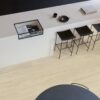 виниловыи-ламинат-quick-step-bloom-sea-breeze-oak-beige Виниловый ламинат Quick Step Bloom Sea Breeze Oak Beige уложен на полу на кухне, стильный каменный кухонный остров и стулья.