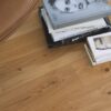 tammiparketti–bauwer-boen-casapark-tammi-46-vivo-harjattu-oljyvahattu-138mm Tammiparketti Bauwerk Boen Casapark tammi 46 Vivo (138 mm), harjattu ja öljyvahattu, asennettuna olohuoneen lattialle – vaaleanruskealla nahalla verhoiltu nojatuoli ja kirjoja lattialla. Luonnollinen Vivo-sävy ja rustiikkinen sorteerus korostavat tammen eläväistä kuviointia.