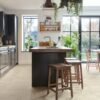 vinyl-tiles-quick-step-illume-pebble-concrete Vinyl tiles Quick-Step Illume Pebble concrete installed on a kitchen floor. Kitchen furniture with an island, rustical style stools next to it.