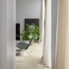 vinylboden-betonoptik-quick-step-illume-pebble-concrete Vinylboden in Betonoptik Quick-Step Illume Pebble Concrete, verlegt auf dem Wohnzimmerboden – schwarze Lederstühle, luftige Vorhänge und eine Zimmerpflanze.