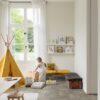 vinylboden-stein-quick-step-oro-concrete-rock Vinylboden in Steinoptik Quick-Step Oro Concrete Rock, verlegt auf dem Boden eines Kinderzimmers – gelbes Tipi-Zelt im Indianerstil, Spielzeugkiste, Sitzkissen sowie Tisch mit Stühlen; ein Kind nimmt ein Spielzeug aus der Kiste.