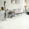 Vinylboden Stein Quick Step Oro Marble Carrara White im Wohnzimmer verlegt heller Carrara Marmor Look in Weiß mit feiner grauer Maserung braune Stühle mit Lederbezug runder Tisch und eckiger Tisch mit goldener Tischleuchte