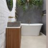 Vinylboden in Betonoptik Quick-Step Illume Oyster Concrete, verlegt im klassisch eingerichteten Badezimmer – freistehende Badewanne, Badmöbel mit Aufsatzwaschbecken auf Betonplatte sowie Wandarmaturen und Wannenmischer in Bronzeton.