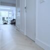 Herringbone parquet Bauwerk Monopark Oak Natur 15 Farina installed in a hallway with white doors and skirting boards, living room in the background